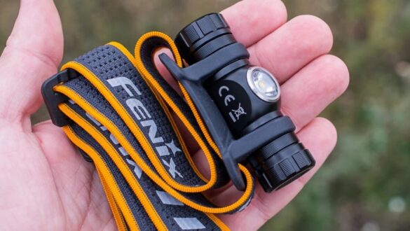 Ліхтарик Fenix HM23 з кріпленням та еластичним ремінцем у руці людини, фон злегка розмитий.