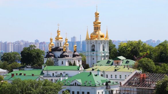 Київська лавра з золотими куполами, зеленою дахами та розкішним ландшафтом на фоні сучасної архітектури столиці України.