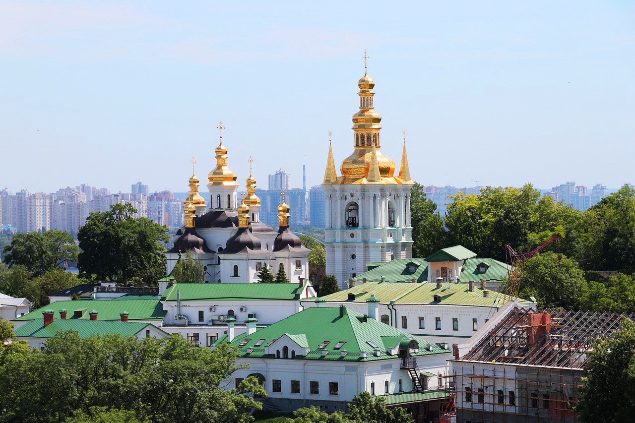 Київська лавра з золотими куполами, зеленою дахами та розкішним ландшафтом на фоні сучасної архітектури столиці України.