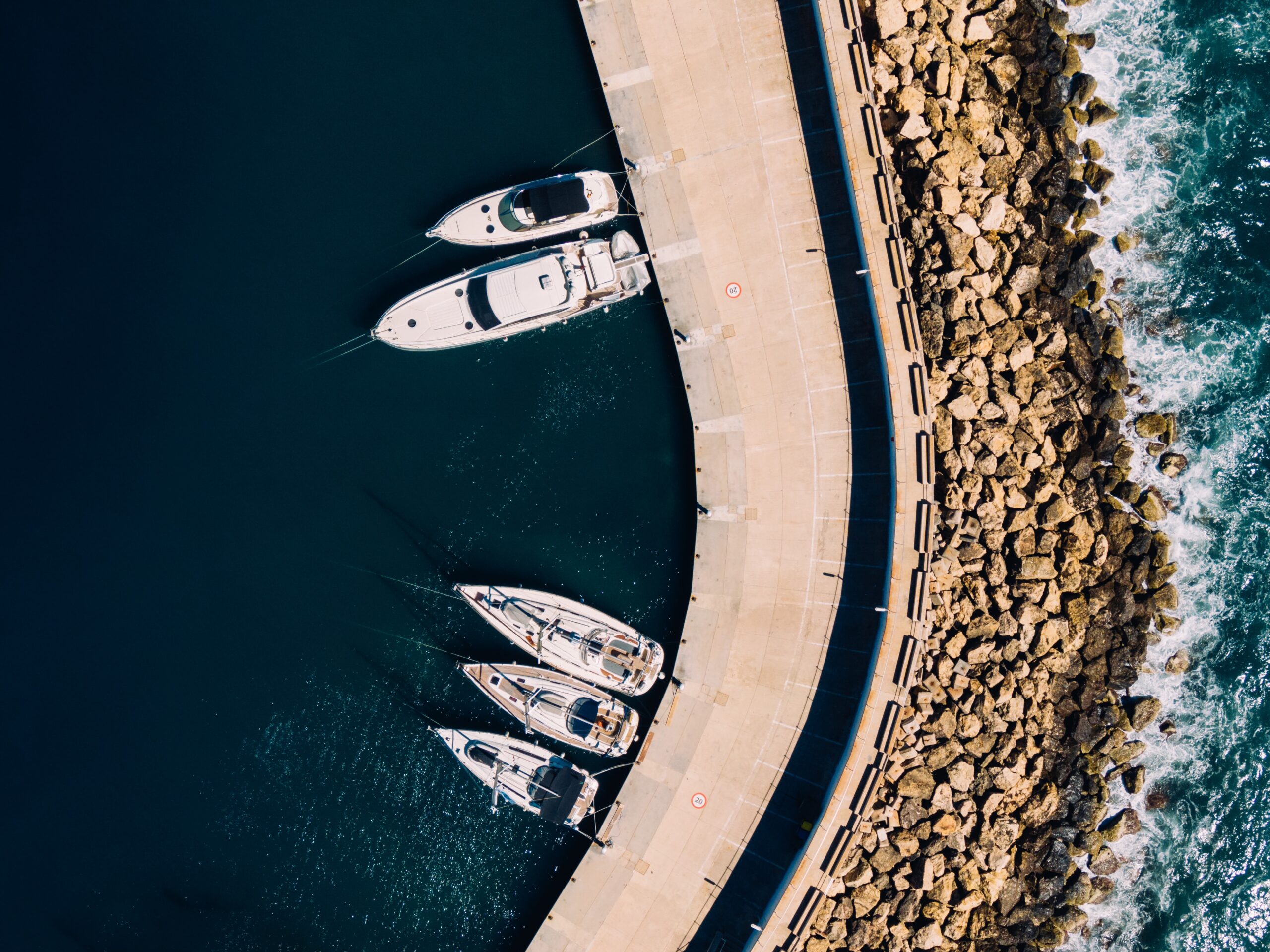 Aerial overhead shot of white sailboats docked on the coast of the ocean