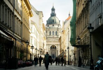Вулиця з пішоходами, оточена історичною архітектурою, в центрі якої видно величну церкву з куполом.