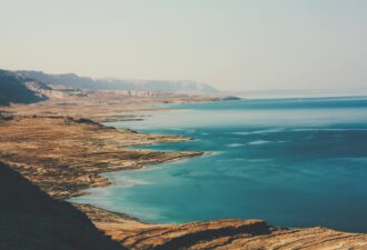 Краєвид Мертвого моря з ясним блакитним небом, піщаними пляжами та скелястими березами, відомий своєю унікальною природною красою та високим вмістом солі.