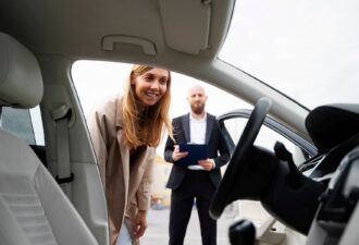 Жінка оглядає салон автомобіля, за нею стоїть чоловік з планшетом, що надає інформацію про авто.