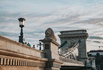 Міст Сечені в Будапешті з левом на перилах та сучасними ліхтарями на фоні неба.