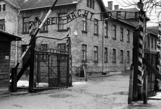 Ворота історичного концентраційного табору, з написом про працю, сріблястю проходу на фоні старих brick будівель, що відображає важливу частину історії.