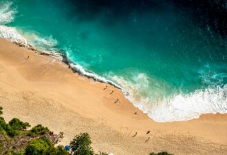 Пляж з золотистим піском та бірюзовим морем, людина прогулюється по узбережжю, хвилі ніжно накочуються на берег. Вид зверху.
