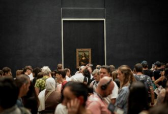 Великі черги туристів у музеї, що захоплено розглядають знамените полотно «Мона Ліза» Леонардо да Вінчі, виставлене на фоні темної стіни.