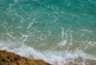 Бірюзові морські хвилі накочуються на скелястий берег, утворюючи білу піну на воді.