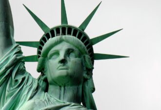Крупний план обличчя Статуї Свободи на тлі світлого неба.
