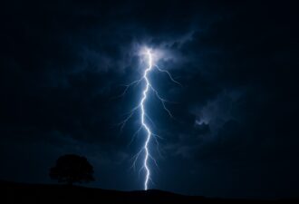 Яскрава блискавка вночі розсікає темне небо, освітлюючи силует самотнього дерева на горизонті.